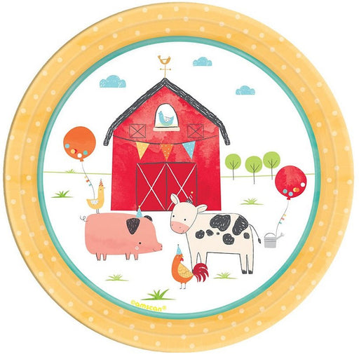 Round paper plate with a farm party theme. The illustration shows a red barn with bunting, a pig, cow, rooster, and chickens wearing party hats, along with balloons and trees in the background. The rim of the plate is yellow with white polka dots.