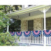 Patriotic bunting decorations in red, white, and blue with stars, displayed along a white porch railing of a brick house.