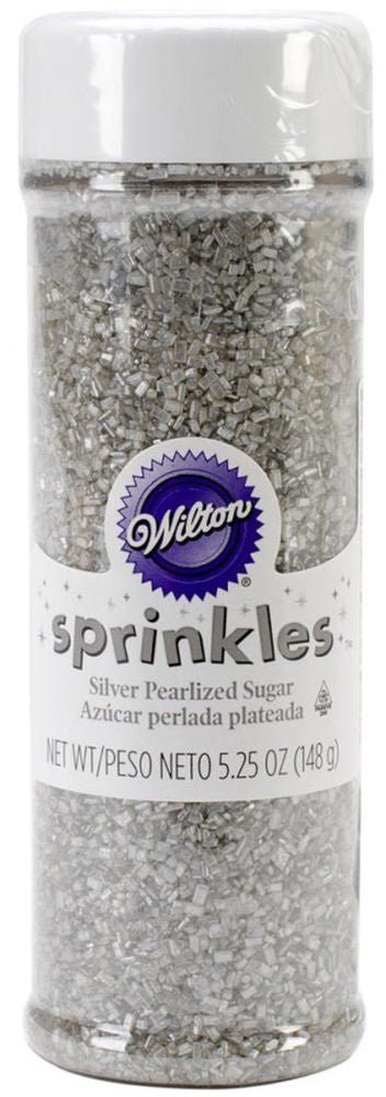 Wilton brand container of silver pearlized sugar sprinkles, labeled in English and Spanish, with a white lid and clear body showing the metallic silver sugar crystals inside. Net weight: 5.25 oz (148 g).