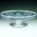 Clear glass cake platter with a scalloped edge and starburst pattern on the surface, elevated on a faceted pedestal base.